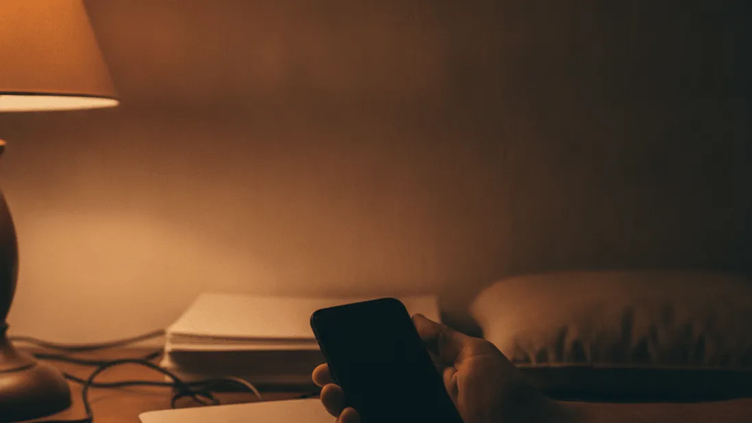 A hand holds a phone with a dark screen, resting on a counter next to a glowing Wi-Fi router.