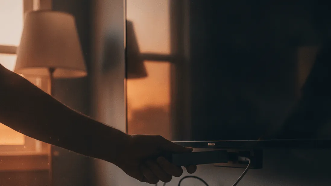 A person's hand plugs a streaming stick into an HDMI port on a television in a dimly lit room.